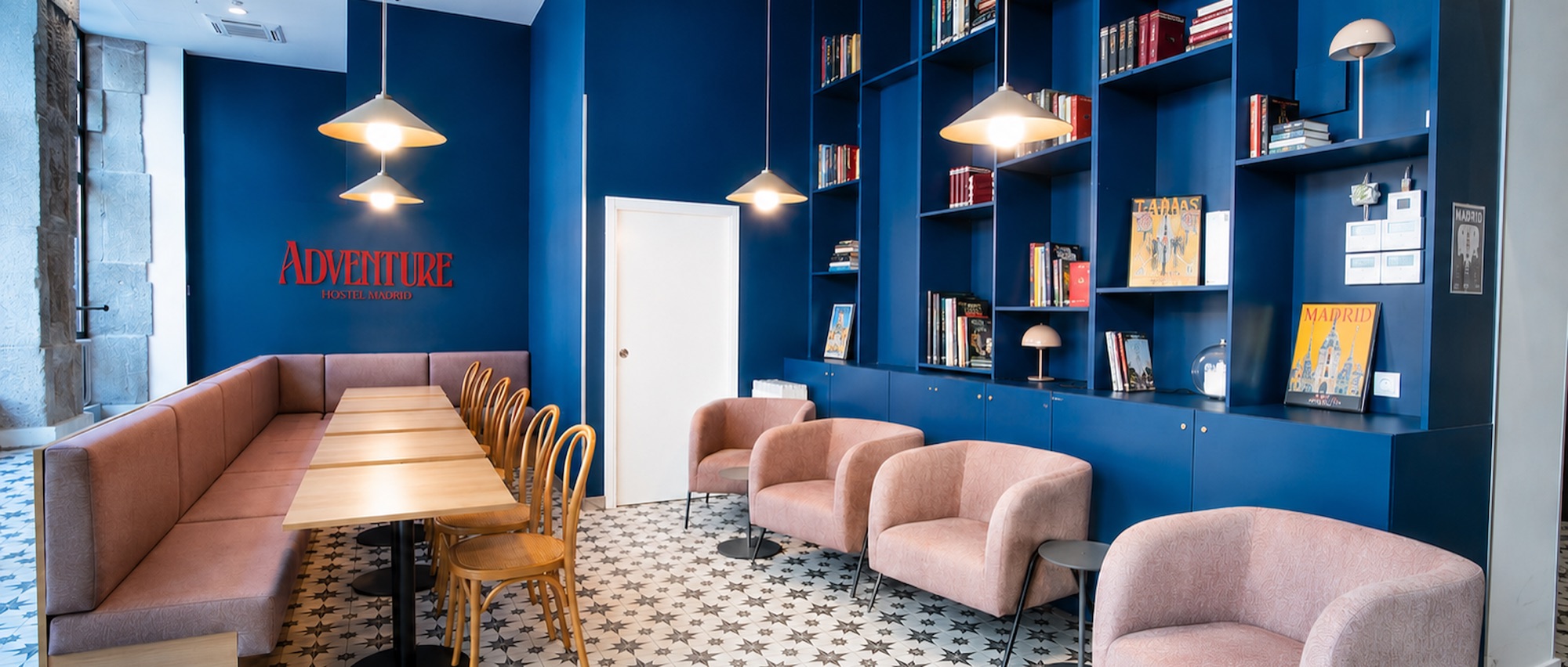 Adventure Hostel lounge with a blue wall, bookshelves and the logo on the wall