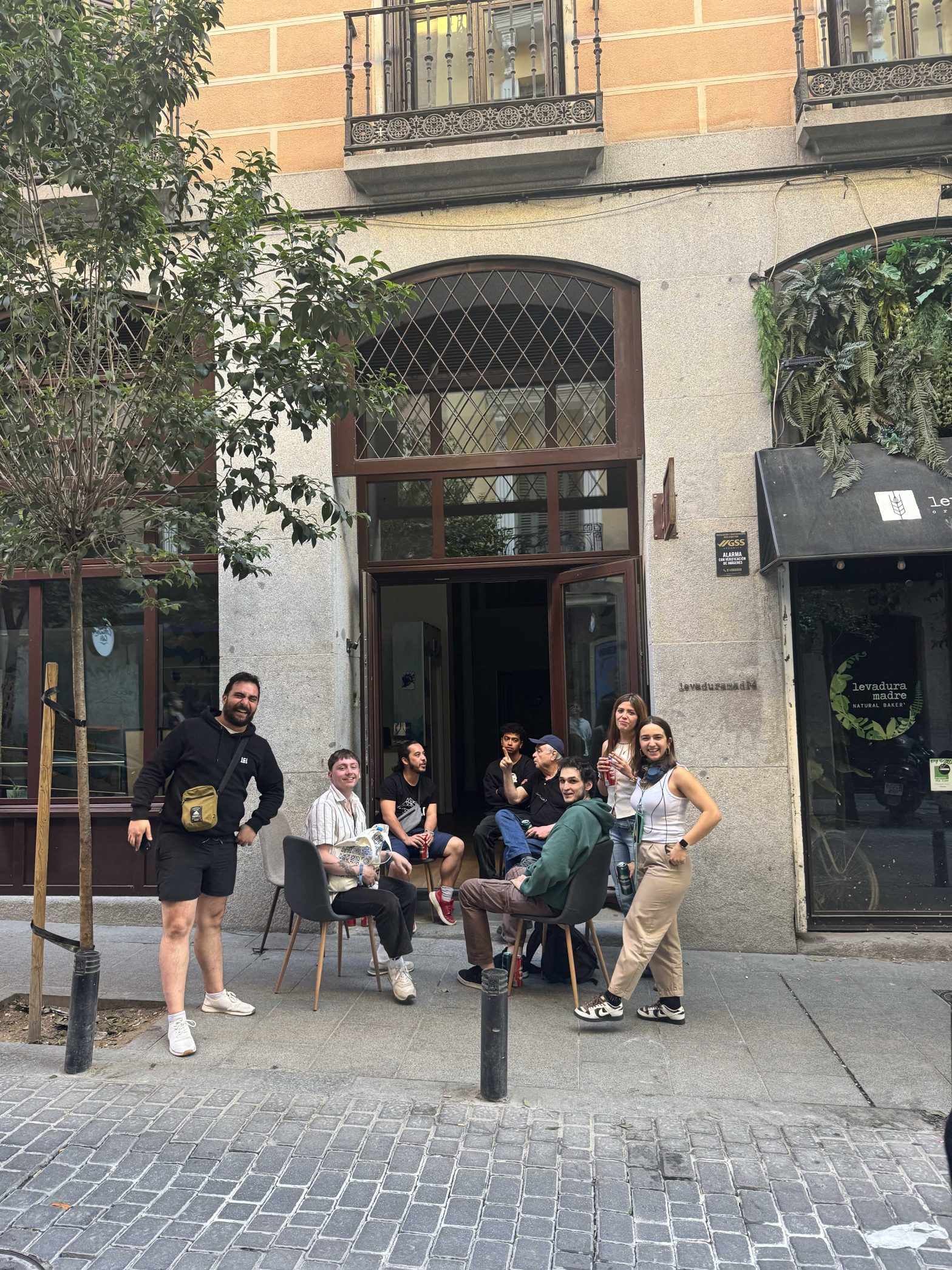 Grupo de personas sentadas en la acera de Adventure Hostel Madrid durante un apagón, con ambiente relajado y natural.