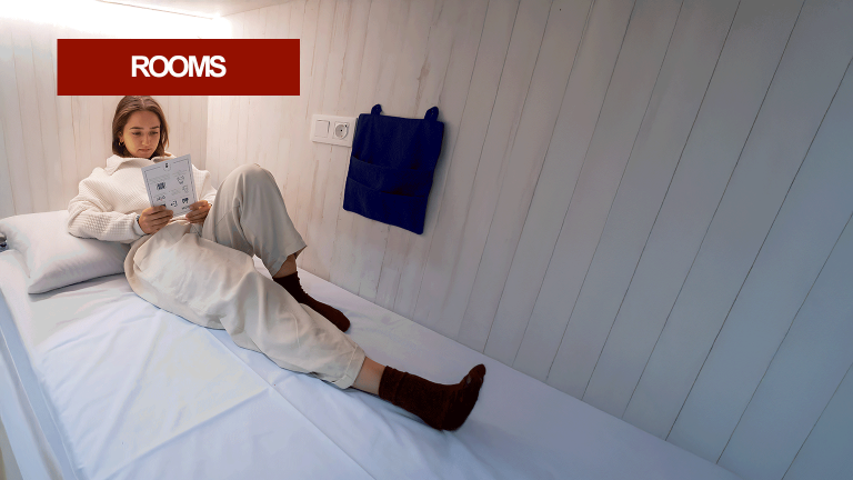 Woman reading while lying on a cozy bed in a modern hostel room.